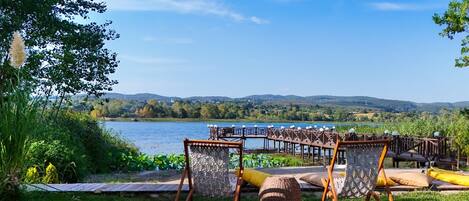 An outdoor seating area with chairs and a table, overlooking a lake and hills.