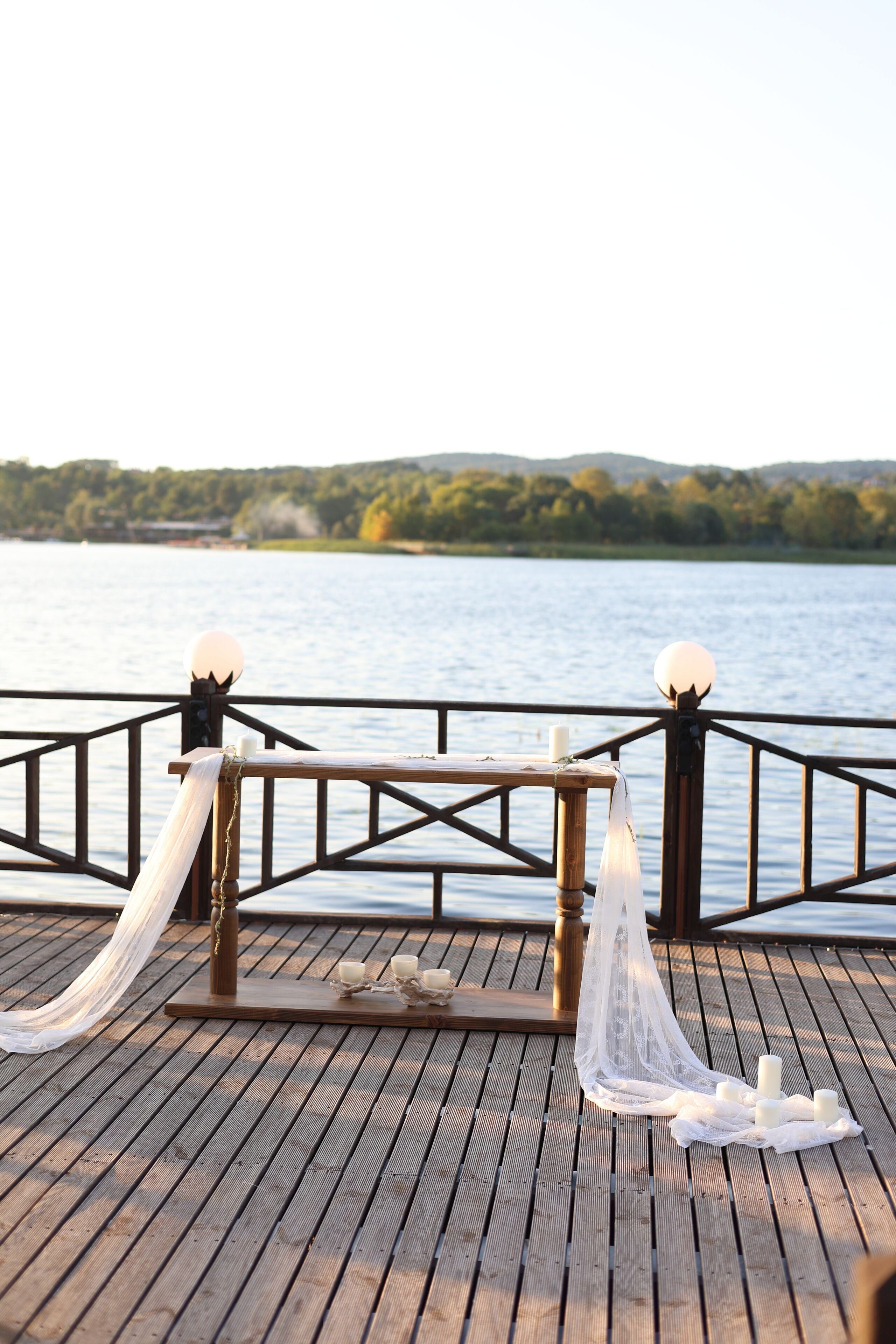 A wooden deck with a railing, candles, and a white cloth.