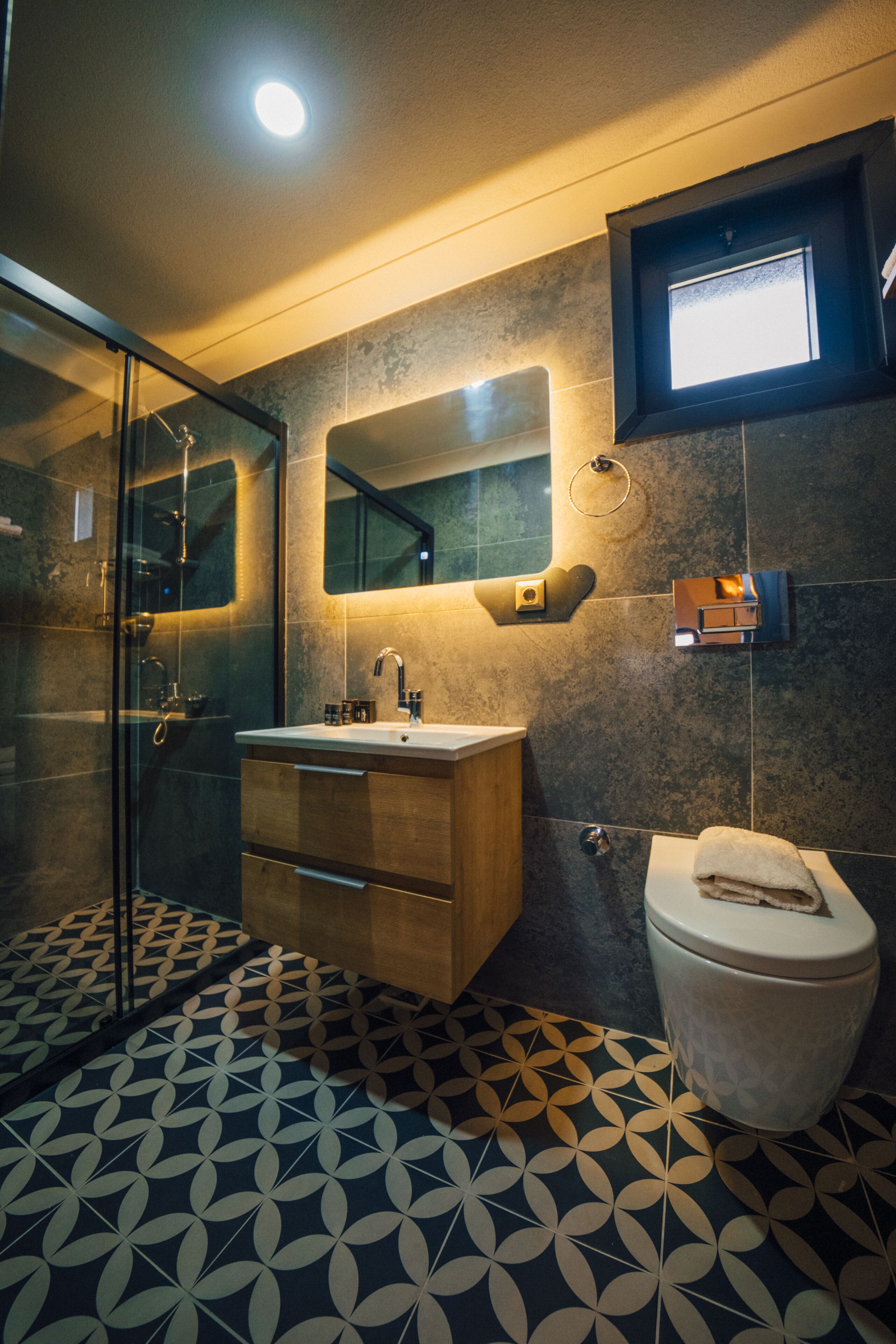 A modern bathroom with a glass shower enclosure, a wooden vanity, a white sink, and a toilet.