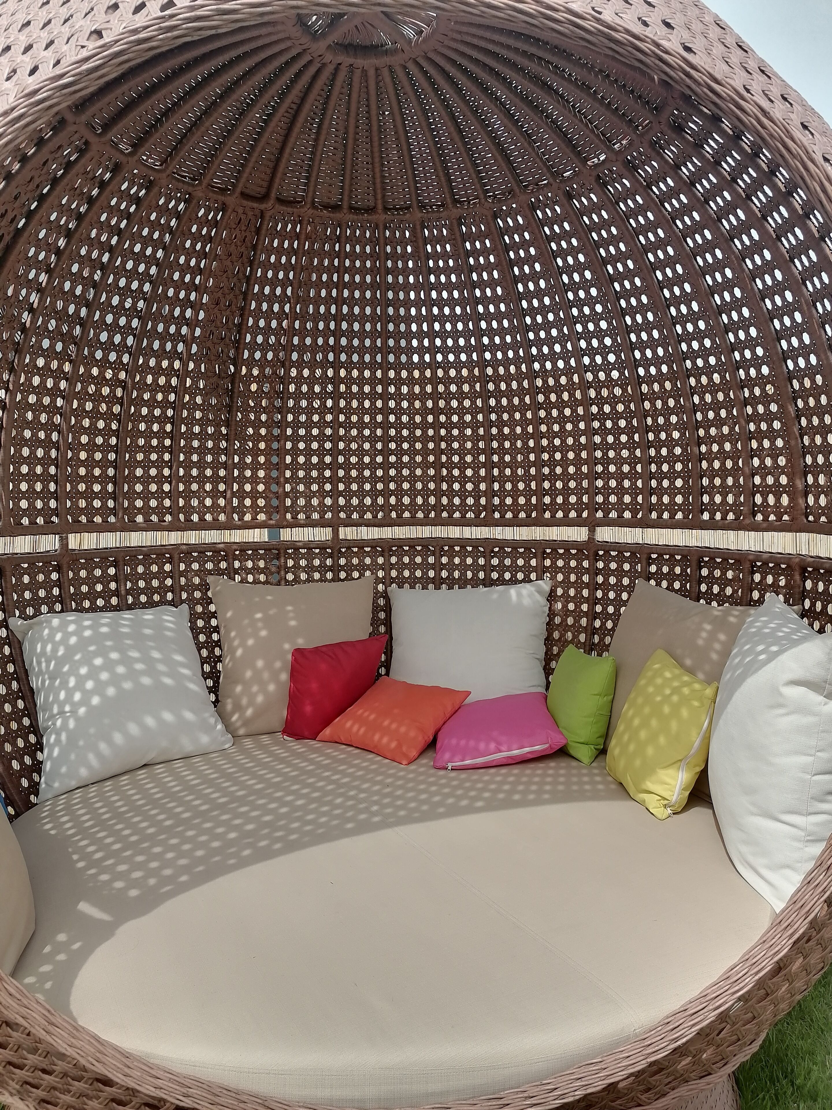 A round, woven outdoor seating area with multiple cushions in various colors.