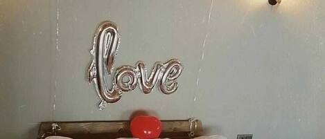 A bedroom with a bed, balloons, and a 'Love' sign on the wall.