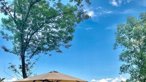 A lakeside patio with a wooden deck, a pergola with an umbrella, and a chair with a basket. - Vital Göl (Sapanca)