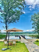 Une terrasse au bord du lac, avec une plateforme en bois, une pergola dotée d’un parasol et une chaise avec un panier.