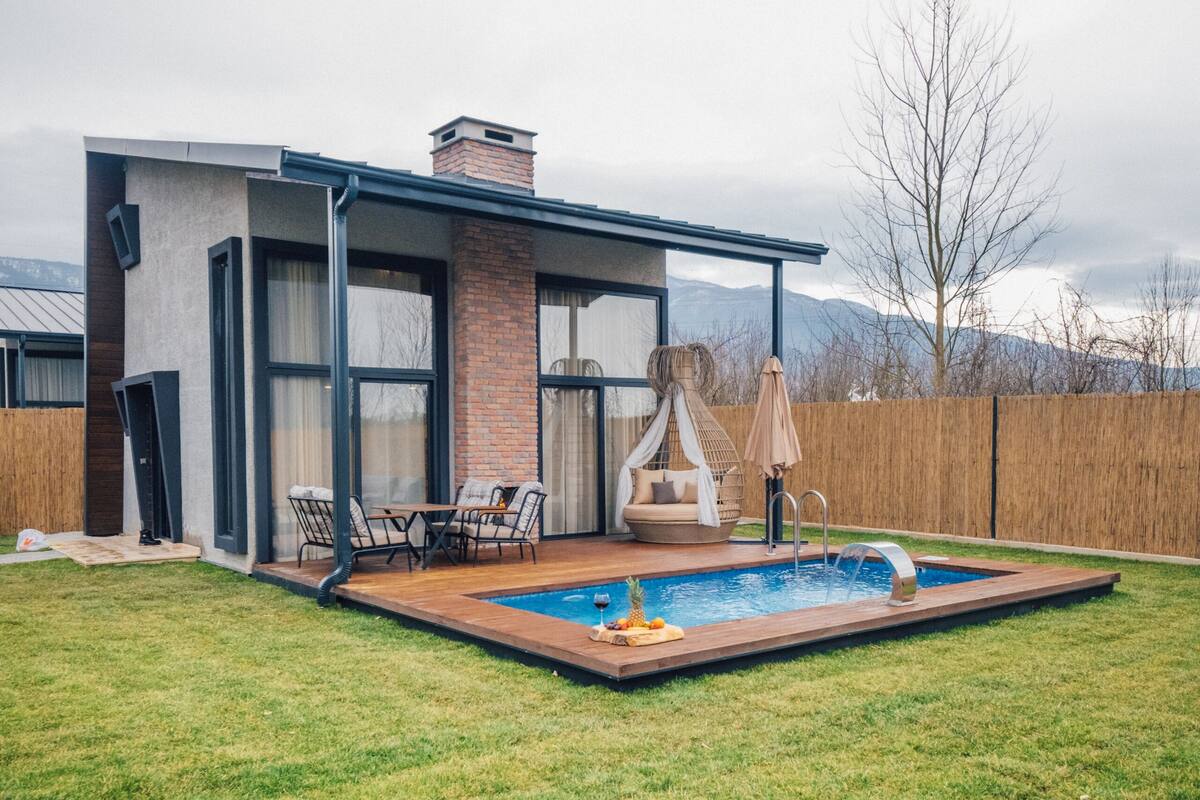 A modern house with a swimming pool, outdoor seating, and a view of mountains.