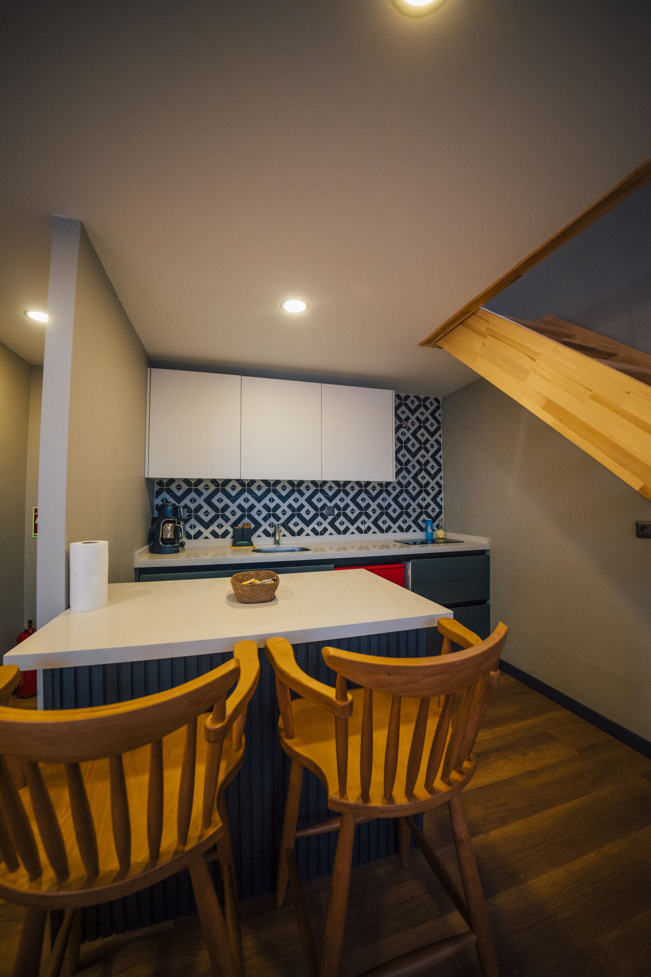 A kitchen with a white countertop, two wooden chairs, and a patterned backsplash.