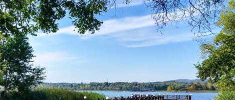 An outdoor seating area with chairs and tables, overlooking a lake with a dock and boats.