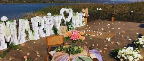 A wedding setup with a wooden deck, a chair, a table with a green plate, and a backdrop with 'MARRY ME' letters.