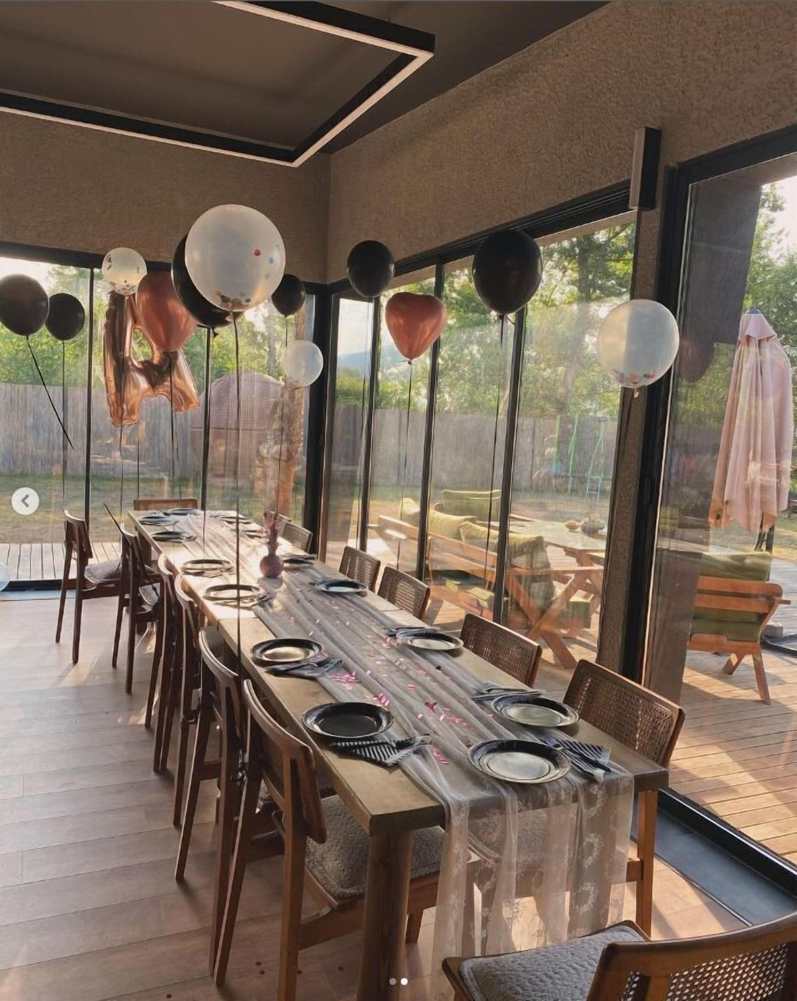 A dining area with a long table set for a meal, surrounded by chairs, and balloons hanging from the ceiling.