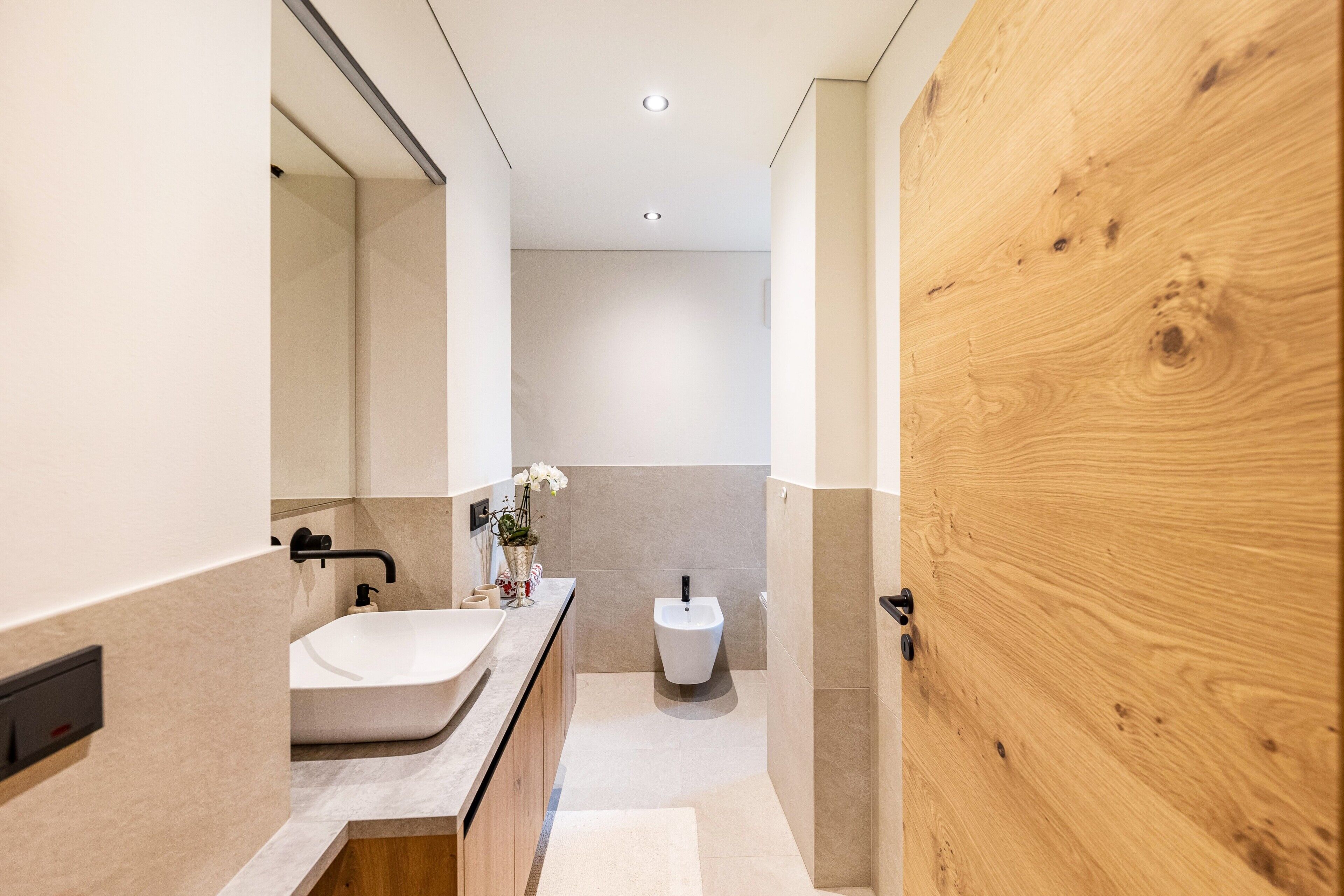 Ein modernes Badezimmer mit Holztür, Waschbecken in Weiß und einem Bidet.