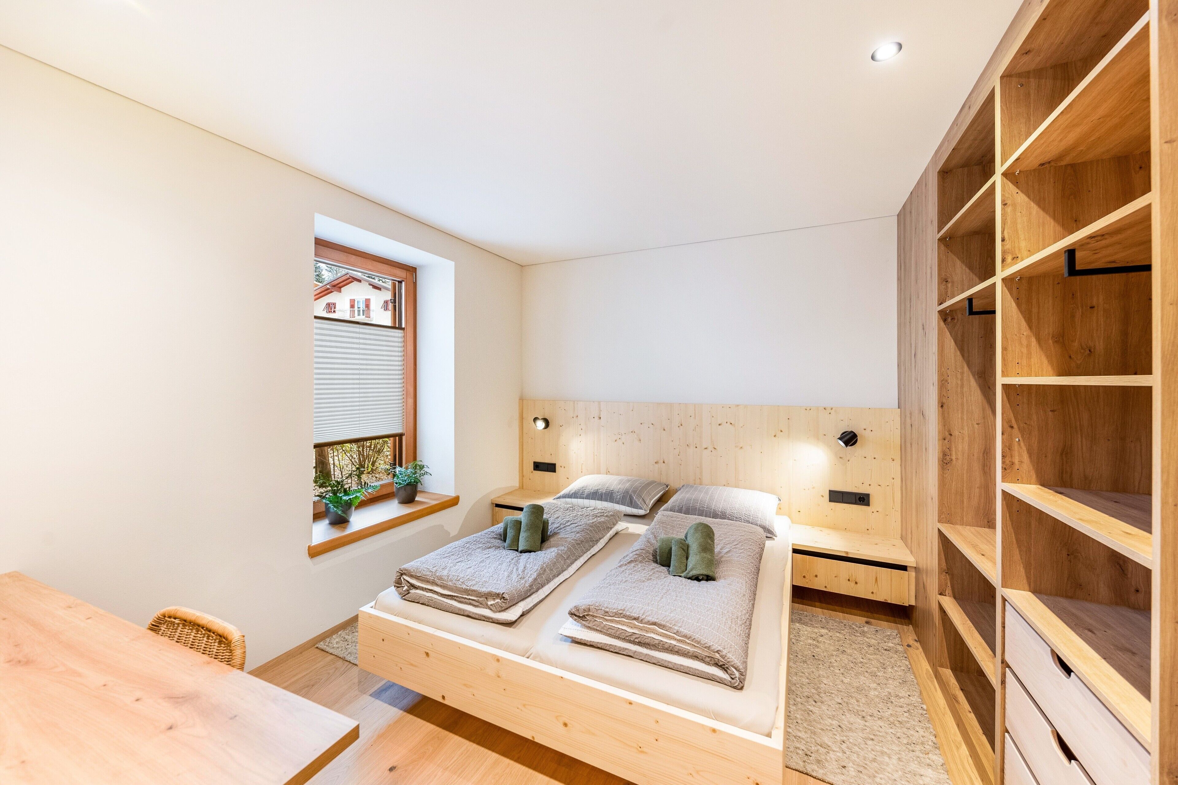 A bedroom with a wooden bed, a window with a view, a wooden desk, and built-in shelves.