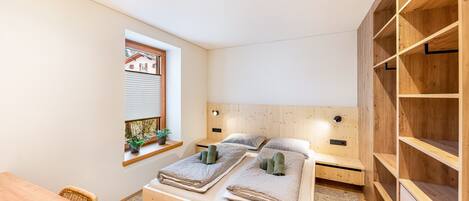 A bedroom with a wooden bed, a window with a view, a wooden desk, and built-in shelves.