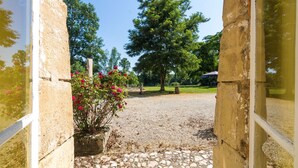 A stone pathway leading to a building with a large tree and flowering plants. - Castle in Chaleix with Pool and Views (Chalais)