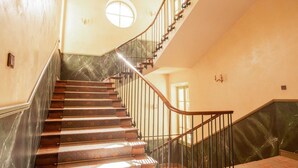 Uma escadaria imponente com degraus de mármore e corrimão curvo, que leva a um patamar com janela circular.
