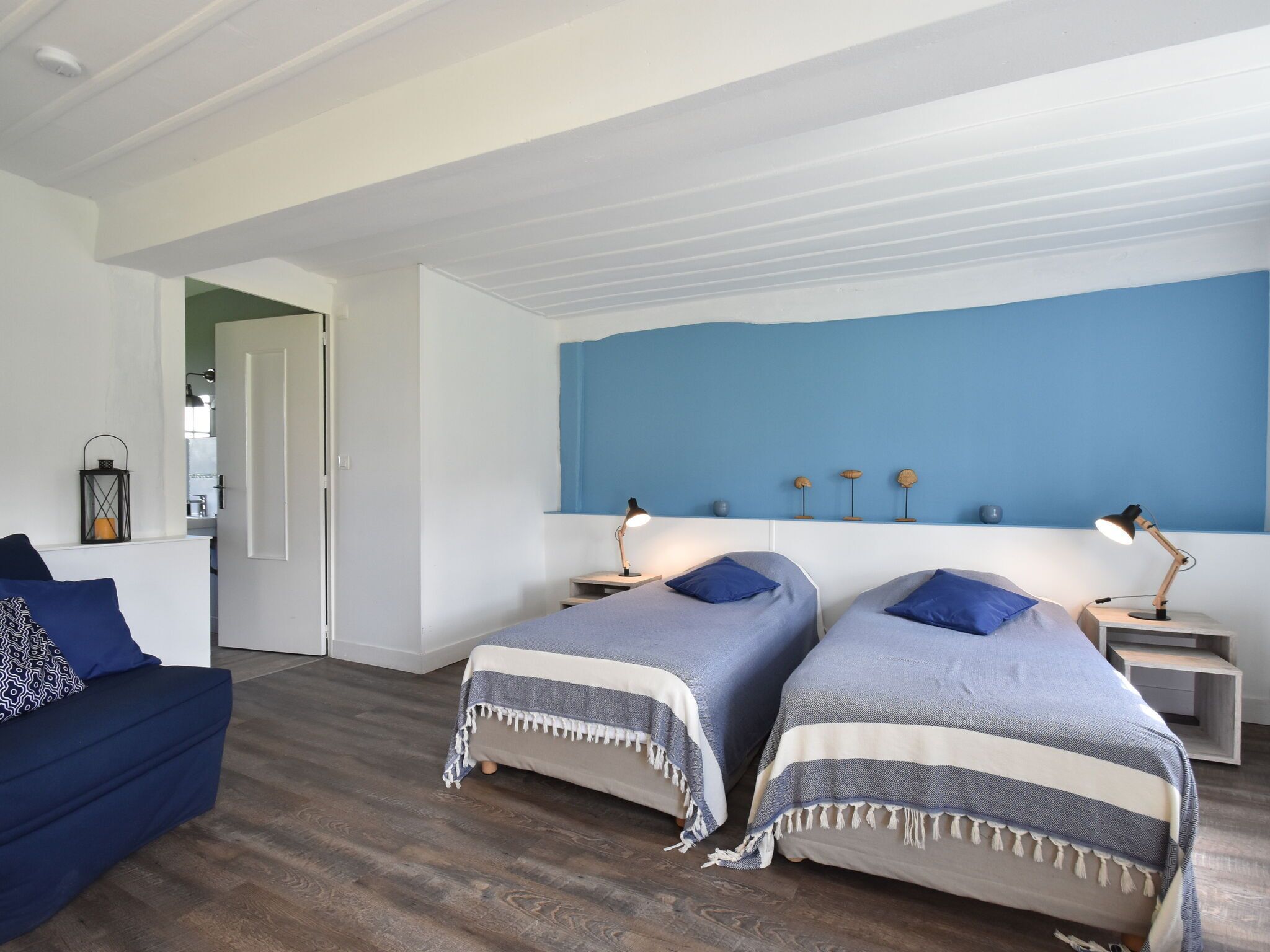 Un dormitorio con dos camas, un sofá y una kitchenette al fondo.