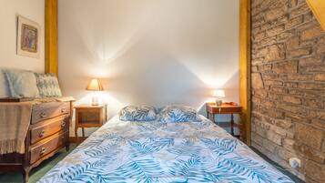 Ein Schlafzimmer mit einem Bett, einer Holzkommode, zwei Nachttischen mit Lampen, einer Wand mit Steinmusterung und einem gerahmten Bild.