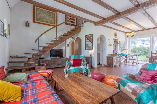 A spacious living area with a wooden staircase, a sofa set, a dining table, and a television.