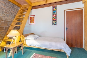 A room with a wooden ladder, a bed, a chair, a table, and a door.