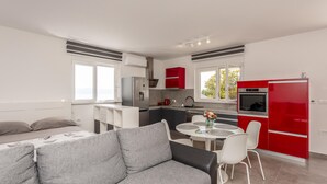 Een moderne keuken met een rode koelkast, een roestvrijstalen fornuis en een witte gootsteen. Er is een eethoek met een ronde tafel en witte stoelen.