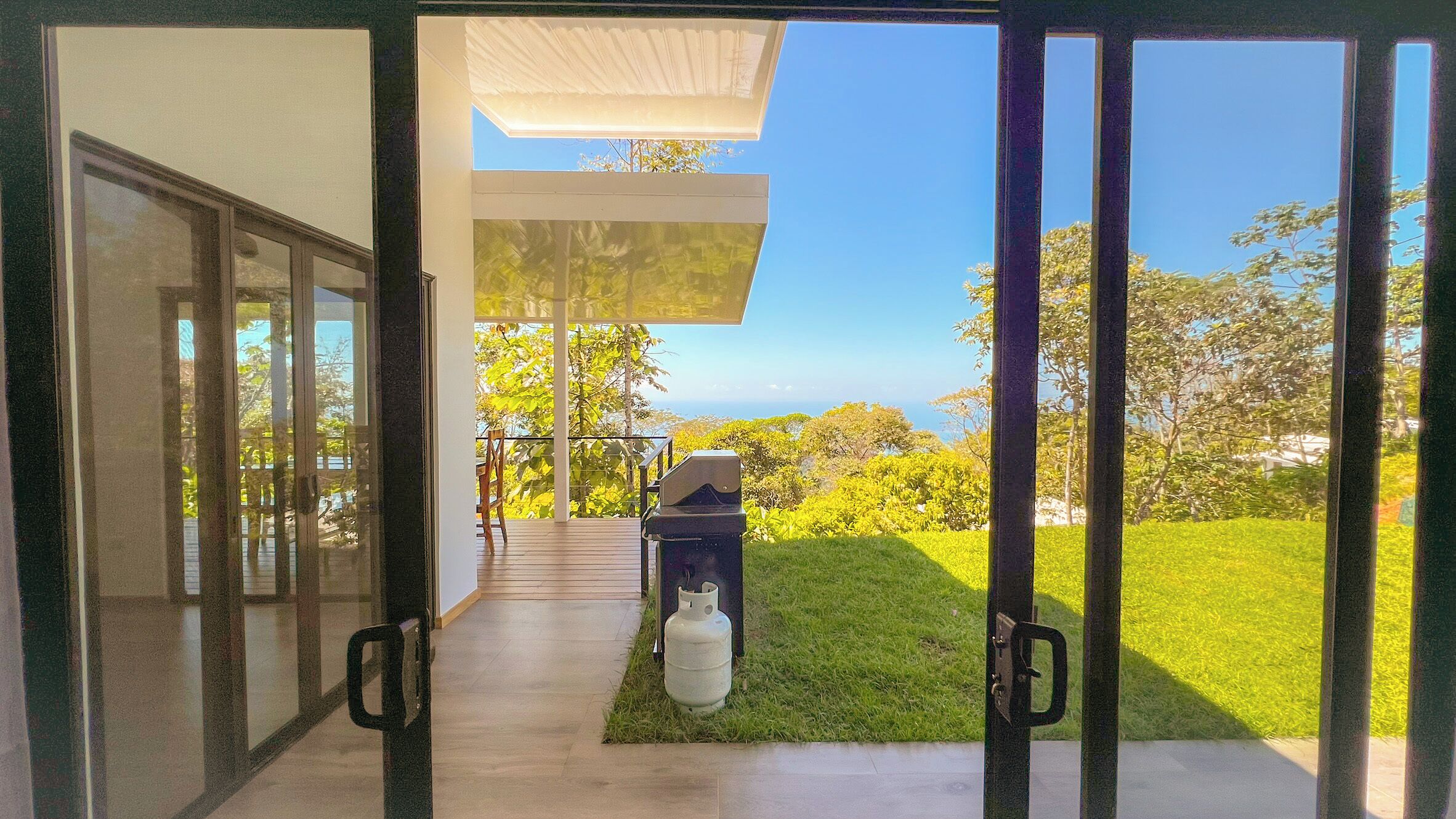 A modern house with a glass door leading to a patio area with a barbecue grill and a gas cylinder.