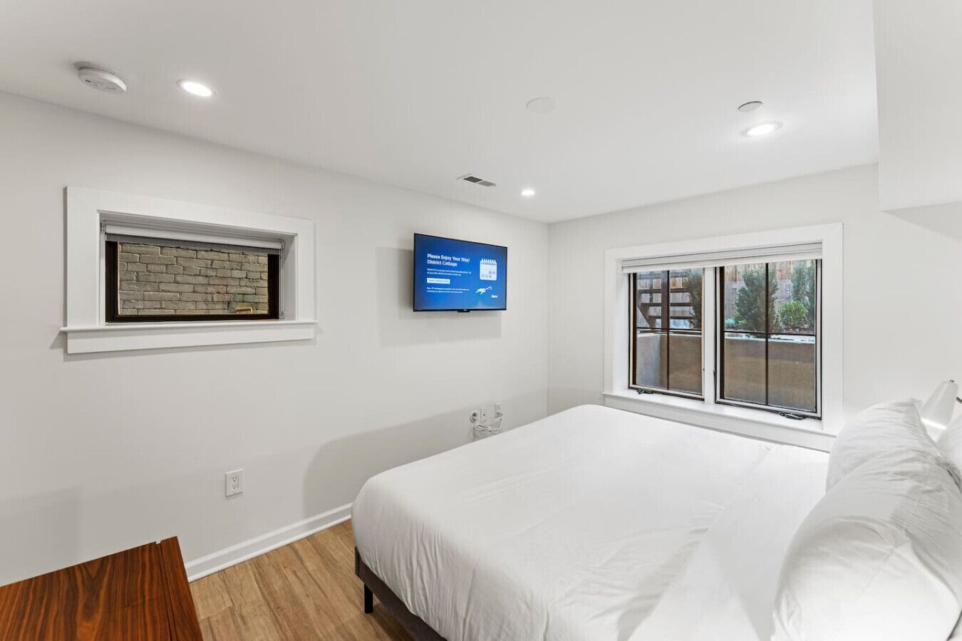 A modern bedroom with a large bed, a television mounted on the wall, and a window providing a view of the outdoors.