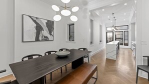 A modern dining area with a long table, benches, and a contemporary chandelier. - The Lincoln | Entire 7BR DC Rowhome | Sleeps 14 (Washington)