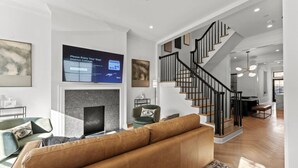A modern living room with a fireplace, a staircase, and a dining area. - The Lincoln | Entire 7BR DC Rowhome | Sleeps 14 (Washington)