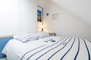 Et soveværelse med en seng, et natbord, en lampe og et billede i ramme på væggen.