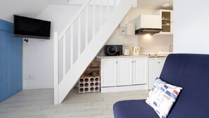 A compact living space with a staircase leading to a kitchen area, a flat-screen TV mounted on the wall, and a blue sofa with a patterned pillow. - Apartment 'Guillaume' with Sea View (tregunc)