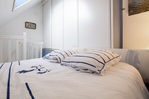 A bed with striped bedding, a white headboard, and a small picture frame on the wall. - Apartment 'Guillaume' with Sea View (tregunc)