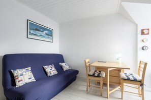 Et værelse med en blå sofa, et træspisebord og stole, et billede i ramme på væggen og et ur på væggen.