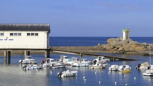 A white building with 'SAUVETAGE EN MER' signage, a dock with boats, and a lighthouse in the background. - Apartment 'Guillaume' with Sea View (tregunc)