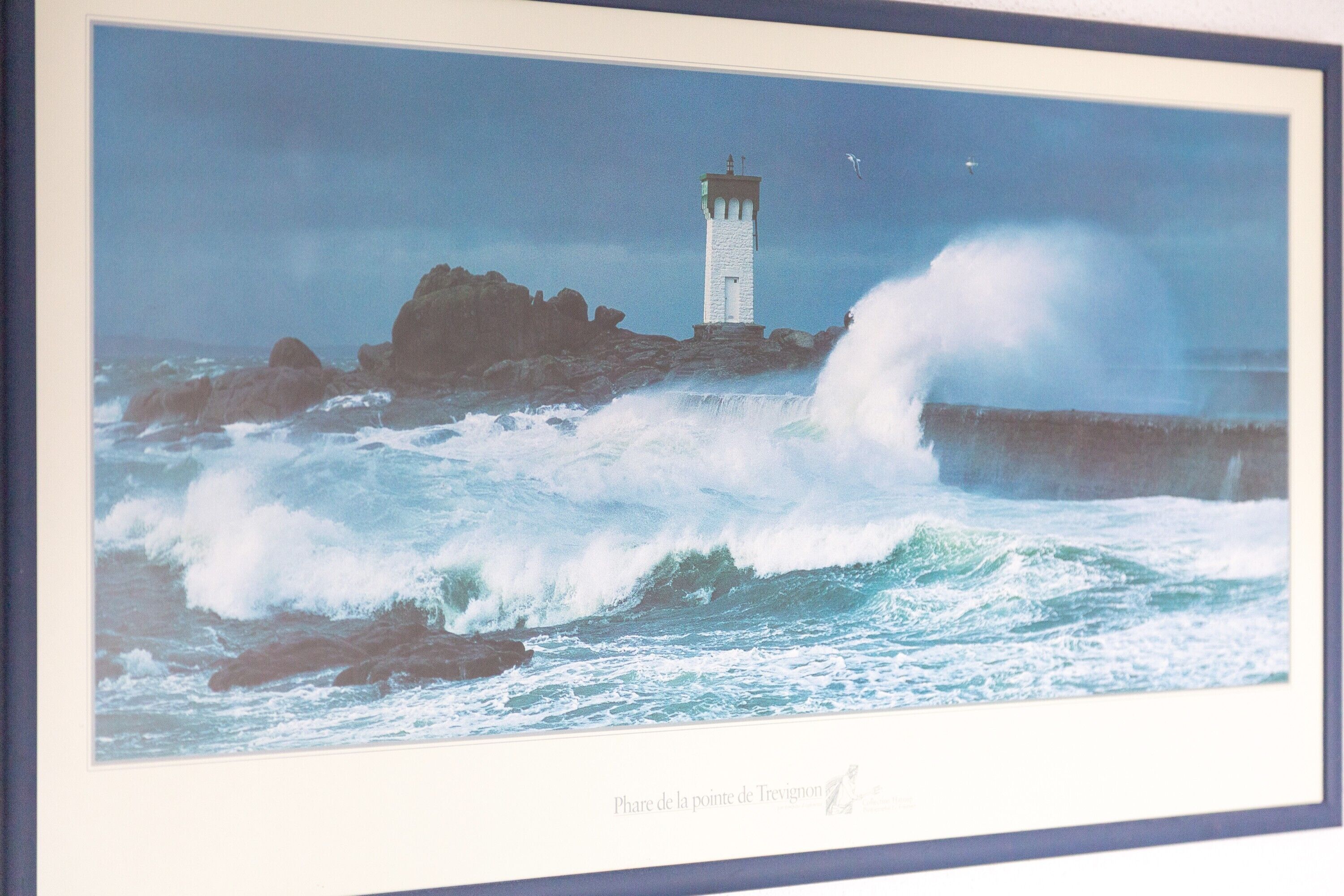 A framed photograph of a lighthouse on a rocky shore with waves crashing against it.