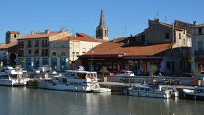 A marina with several boats docked, a church with a tall spire, and buildings with commercial establishments. - Villa in Saint-Privat-de-Champclos with pool (Barjac)