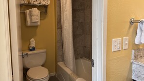 Une salle de bain avec des toilettes, une douche avec un rideau blanc et un porte-serviettes avec des serviettes pliées.