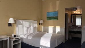 Une chambre d’hôtel avec un lit, des lampes de chevet, un tableau, une salle de bain avec un miroir et un téléphone sur la table de chevet.