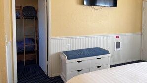 Une chambre avec un lit superposé, une table de chevet avec des tiroirs, un téléviseur fixé au mur et un radiateur.