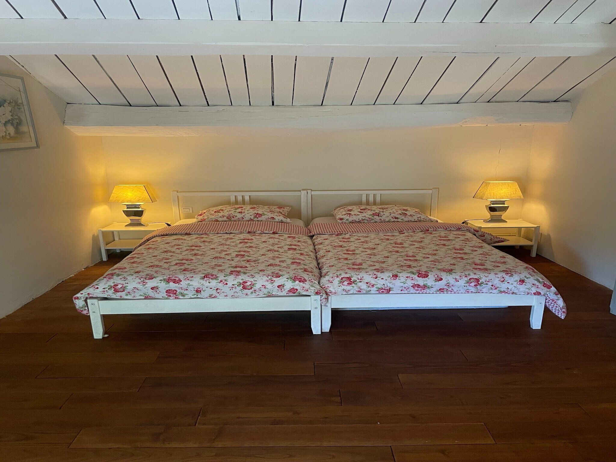 Ein Doppelbett mit Blumenmuster auf der Bettwäsche, zwei Nachttische mit Lampen und eine Holzbalkendecke.