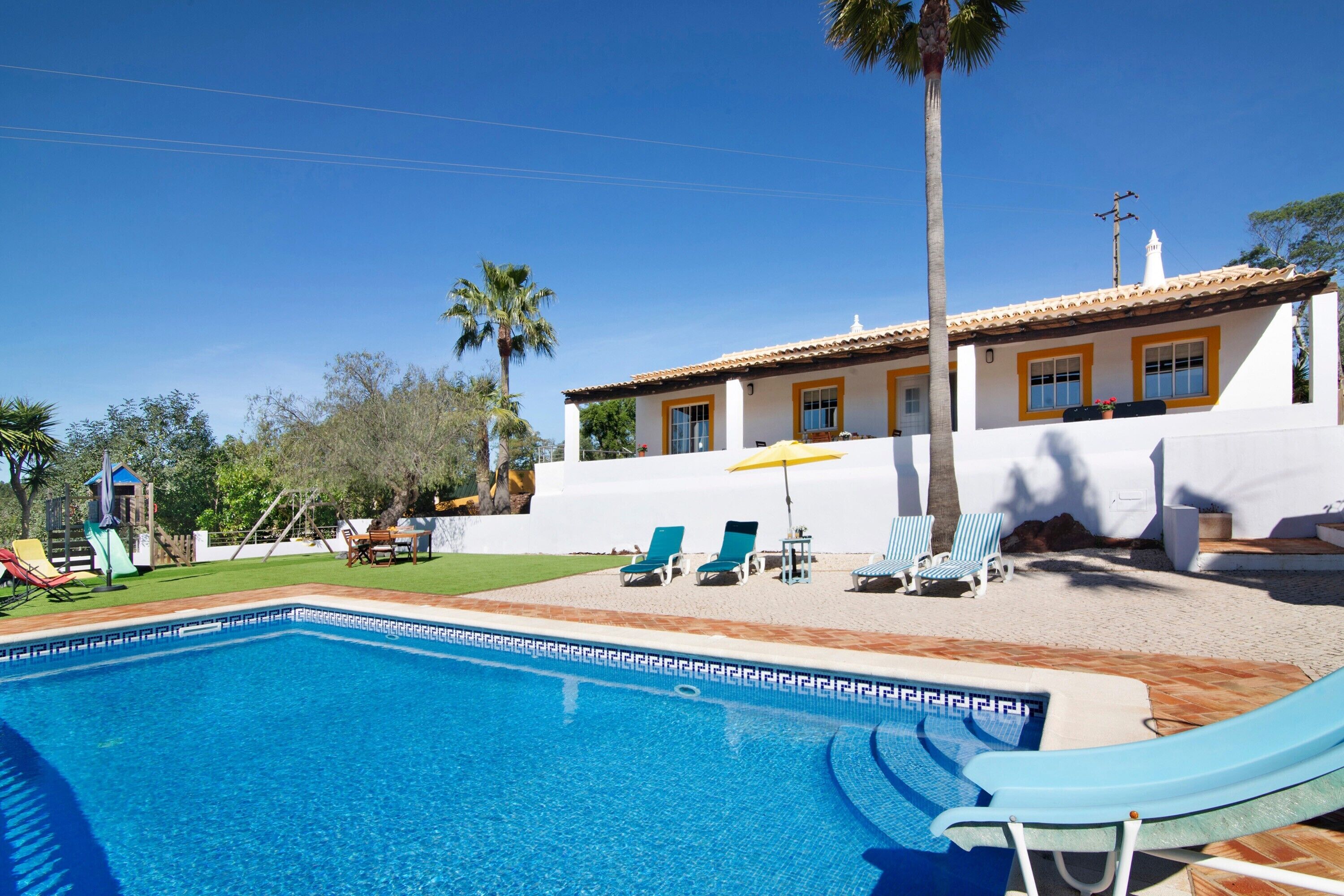 Una piscina amb gandules, una palmera i un edifici amb adorns grocs.