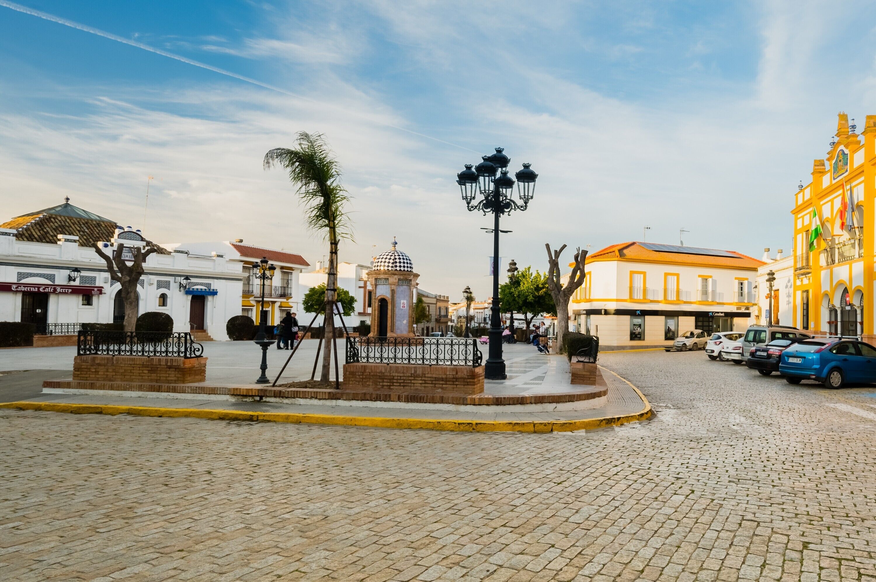 Una calle empedrada con un monumento central, una palmera y edificios de arquitectura tradicional.