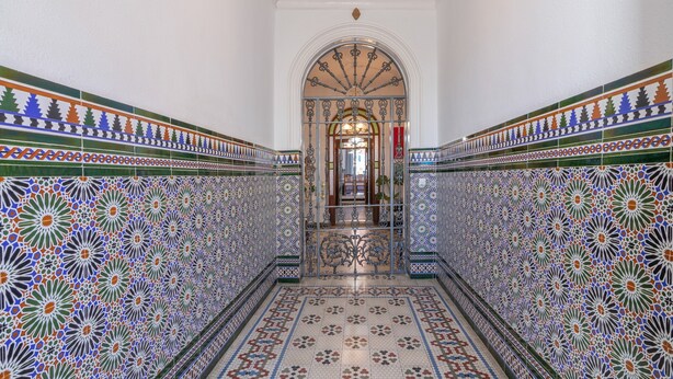 Un couloir orné de motifs complexes en mosaïque, un arc central et un lustre.