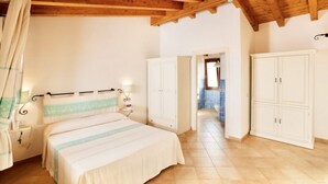 A bedroom with a wooden ceiling, a bed with a striped bedspread, white wardrobes, and a bathroom visible through an open door. - Studio apartment for 2 people of 27 m2 furnished in Sardinian style.Located on the ground floor with veranda and small garden or first floor with balcony.Composed of living room with kitchenette, 2 joinable single beds, bathroom.Endowed of:- TV- air cond (Vignola Mare / Aglientu)