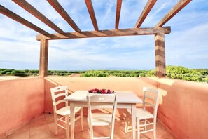 A terrace with a wooden pergola, two white chairs, and a table with a flower arrangement.