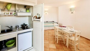 A compact kitchen with a sink, stove, and storage shelves. Adjacent is a dining area with a table and chairs. - Studio apartment for 2 people of 27 m2 furnished in Sardinian style.Located on the ground floor with veranda and small garden or first floor with balcony.Composed of living room with kitchenette, 2 joinable single beds, bathroom.Endowed of:- TV- air cond (Vignola Mare / Aglientu)