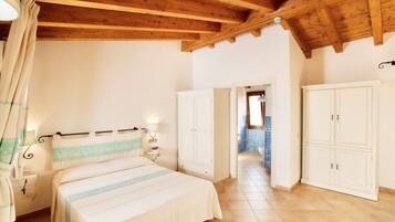Une chambre avec un plafond en bois, un lit recouvert d’une courtepointe à rayures, des armoires blanches et une salle de bain visible à travers une porte ouverte.