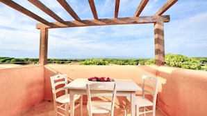 A terrace with a wooden pergola, two white chairs, and a table with a flower arrangement. - Studio apartment for 2 people of 27 m2 furnished in Sardinian style.Located on the ground floor with veranda and small garden or first floor with balcony.Composed of living room with kitchenette, 2 joinable single beds, bathroom.Endowed of:- TV- air cond (Vignola Mare / Aglientu)