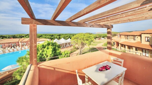 A balcony with a table and chairs, overlooking a pool and a resort area with buildings and greenery. - Studio apartment for 2 people of 27 m2 furnished in Sardinian style.Located on the ground floor with veranda and small garden or first floor with balcony.Composed of living room with kitchenette, 2 joinable single beds, bathroom.Endowed of:- TV- air cond (Vignola Mare / Aglientu)