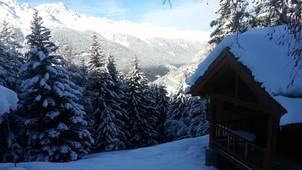 A wooden cabin with a snow-covered roof, surrounded by snow-laden trees and mountains in the background. - Chalet in Huez near Ski Slope (Oz en Oisans)