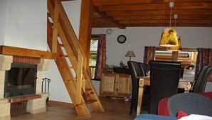 A cozy living room with a fireplace, wooden beams, a dining area, and a staircase. - Chalet in Huez near Ski Slope (Oz en Oisans)