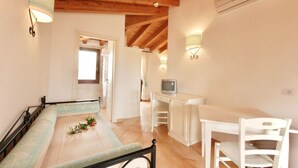 Una habitación acogedora con una cama, un escritorio y una silla. Hay un televisor en el escritorio y una ventana al fondo.