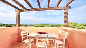 Una terraza con una pérgola de madera, dos sillas blancas y una mesa con un arreglo floral.